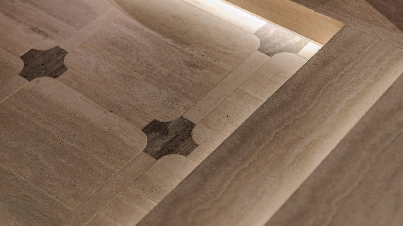 Im Untergeschoss verschmelzen beige- und braunfarbener Travertin, edles Nussholz, metallische Strukturen und feines Leder zu einer harmonischen Einheit. Das Zusammenspiel aus klaren Linien und sanft gerundeten Formen prägt dabei maßgeblich die Atmosphäre und das Geschehen. Angrenzend zur Tanzfläche wurden insgesamt vier massive Sekttische, bestehend aus Travertin Romano Classico (Unterteil) und Travertin Titanium (Oberteil) positioniert, die zum entspannten Verweilen einladen. In Präzisionsarbeit wurden in die Sekttische Vertiefungen sowie konische Aussparungen für Sektkübel eingearbeitet.
