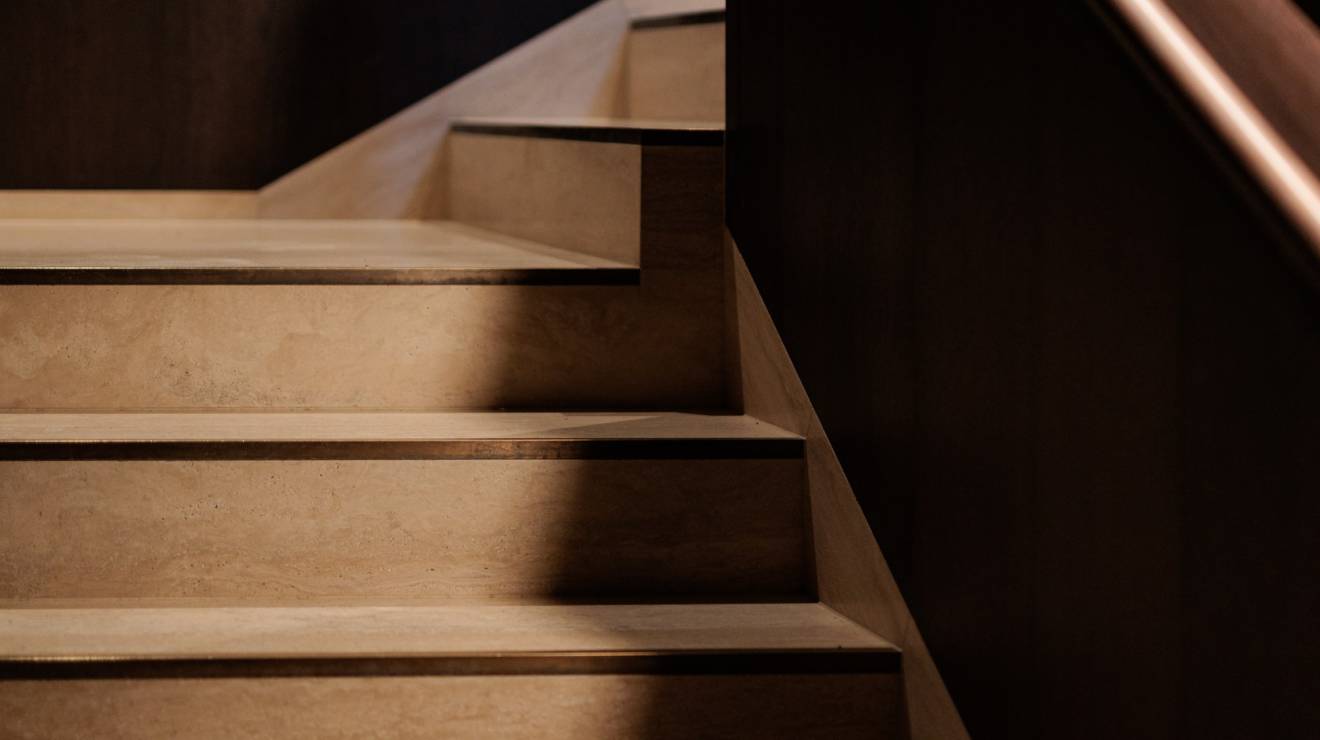 ####Das Treppenhaus besticht durch die Kombination von natürlichem Holz und Travertin, eleganter Beleuchtung und dezenten Messingelementen, die Funktionalität und Design vereinen. Die individuell gefertigten Bischofsmützen ergänzen das Erscheinungsbild harmonisch.