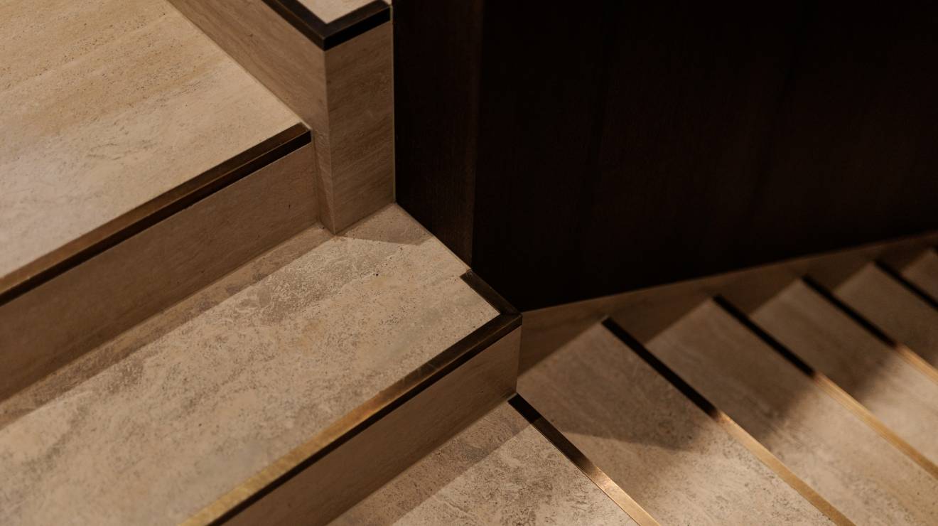 ####Das Treppenhaus besticht durch die Kombination von natürlichem Holz und Travertin, eleganter Beleuchtung und dezenten Messingelementen, die Funktionalität und Design vereinen. Die individuell gefertigten Bischofsmützen ergänzen das Erscheinungsbild harmonisch.